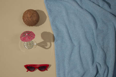 Summer scene with blue beach towel and coconut and red sunglasses and glass with parasol. Minimal concept flat lay.の写真素材