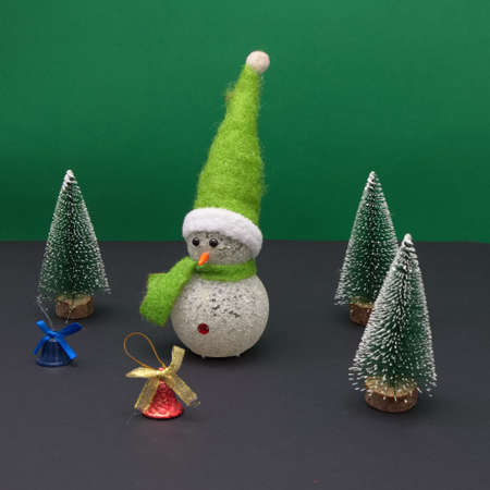 Snowman in a pine forest with New Year's decorations on a green-black background. Minimal scene.の写真素材