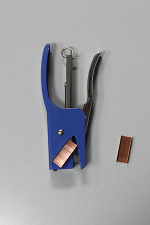 A blue stapler perched atop a shining piece of copper radiates a feeling of purpose and productivityの写真素材