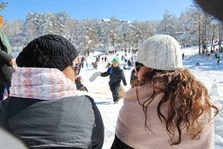 Two friends relax and watch others play in the snow.の写真素材