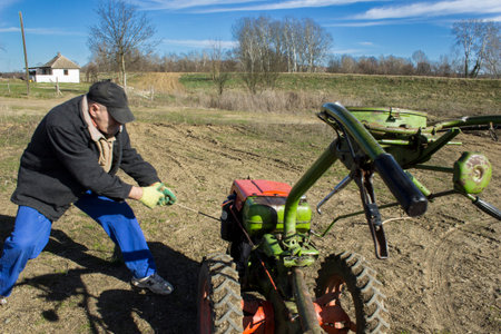 A man stands in the middle of a sprawling field, the sky above him and the earth below his feet, as he pulls a tractor through the grassy terrain, wearing clothing suitable for the rugged outdoor environmentの写真素材