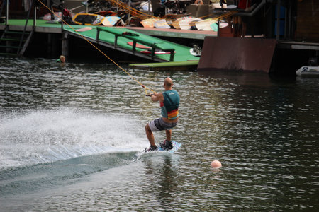 A thrill-seeking man braves the waves, combining style and skill as he rides atop a boat on the shimmering lake, embodying the freedom of outdoor sportsの写真素材