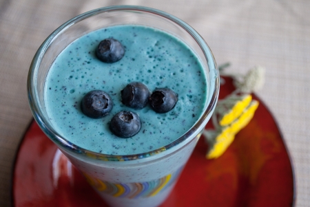 Close-Up of Bright Blue Fresh Blueberry Summer Smoothie with blueberries on top sitting on a red plate の写真素材
