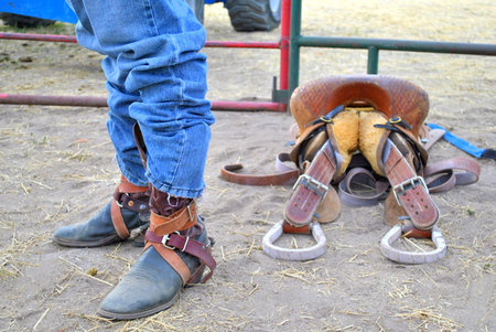 Cowboy wearing cowboy boots and buckles next to staddle at country rodeo 