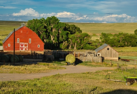 Red bard in rural field with outbuildings and round bale of hayのeditorial素材