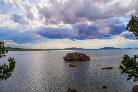 Evening clouds reflected on a mountain lake with mountain range in the backgroud and green fir trees in the foreground の写真素材