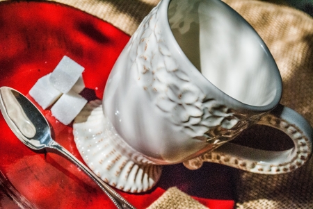 close up of white cup of coffee against a red plate with a silver spoon and burlap napkinの写真素材