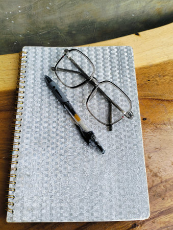 Notebook with pen and glasses on wooden table. professional workspace organization. Top view