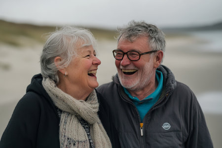 Joyful portrait of an elderly couple with gray hair enjoying laughter together on the beachの素材