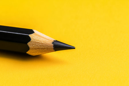 Close up of a black pencil on a vibrant yellow background in a minimalistic photography styleの写真素材