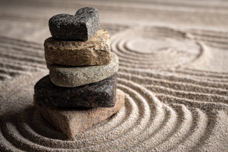 Heart shaped stones stacked in a zen garden with ripples and circular patterns in the sandの写真素材