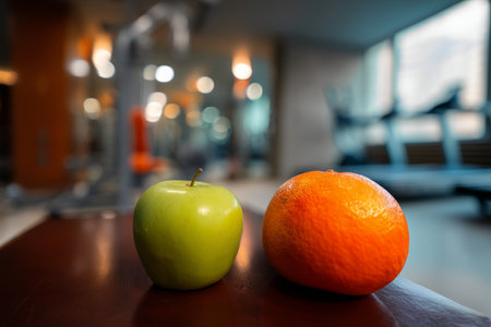 Fresh green apples and red oranges on a table with fitness club background for healthy lifestyleの写真素材