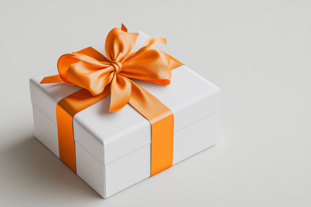 Elegant white gift box adorned with orange satin ribbon and bow on a light gray backgroundの写真素材