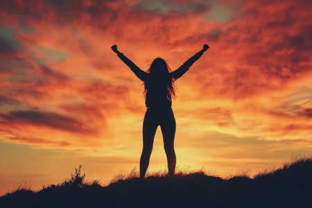 Silhouette of a victorious woman on a hilltop against a stunning sunset sky background