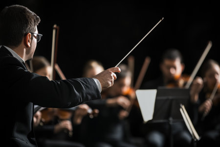 Conductor leading orchestra with baton in focus amidst blurred symphony members on stageの写真素材