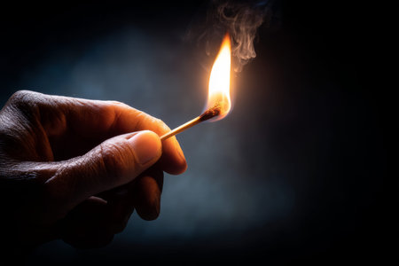 Close up of a hand holding a lit match ready to ignite against an isolated background