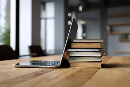 Modern office scene featuring laptop and books on wooden table for online education inspirationの写真素材