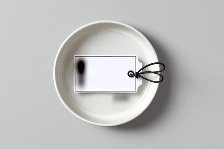 Minimalist flat lay of white rectangular tag with black border on empty round ceramic plateの写真素材