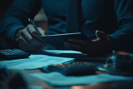 Businessman analyzing documents on tablet with calculator on desk in professional office settingの写真素材
