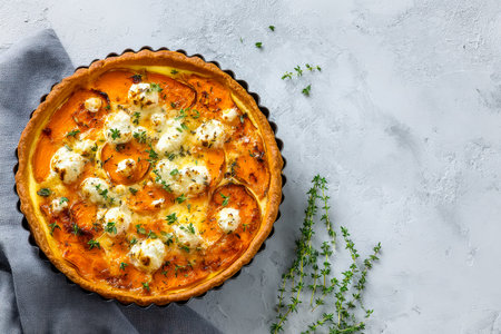 A golden rustic tart topped with juicy tomato slices, melted cheese, and fresh herbs, arranged on a textured gray backdrop for a cozy, inviting feel.の写真素材