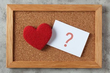 A soft, red heart-shaped plush toy paired with a curious question mark pin on a rustic corkboard, creating a playful and thoughtful mood.の写真素材