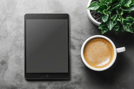 A cozy workspace setup featuring a sleek tablet, steaming coffee in a white mug, and a lush small plant, all on a textured gray surface conveying calmの写真素材