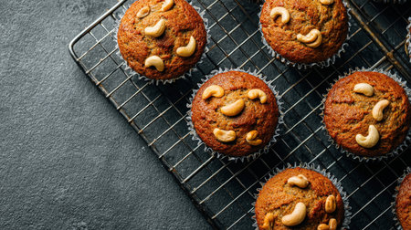 Warm, golden-brown muffins topped with crunchy cashew nuts elegantly arranged on a wire rack, evoking comfort and homemade charm.の写真素材