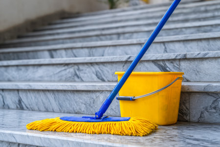 A vibrant yellow bucket and mop rest on polished marble stairs, evoking freshness and readiness for detailed cleaning in elegant surroundings.の写真素材