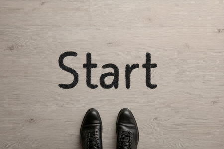 A close-up of sleek black shoes positioned on a pale wood surface, with the bold word 'start' inscribed beneath, evoking readiness and new beginnings.の写真素材