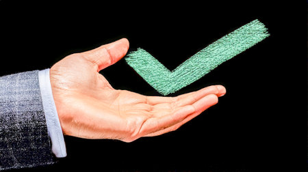 A professional man's hand holds a chalk illustration of a check mark, symbolizing approval or success against a sleek black backdrop.の写真素材