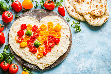 Vibrant, handmade flatbread crafted into a loving heart, topped with ripe cherry tomatoes, fresh greens, and colorful vegetables on a textured woodenの写真素材