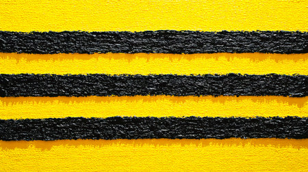 A vivid, tactile surface featuring bold yellow and black parallel stripes with a rough, textured finish ideal for safety, warning, or industrial designの写真素材