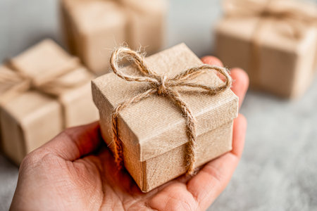 A close-up of a hand clutching a rustic package decorated with twine, set amid a cozy spread of...