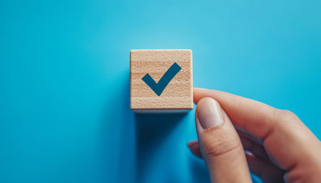 A hand gently grips a wooden emblem featuring a prominent checkmark, set against a vibrant blue...