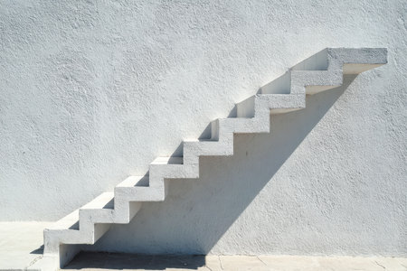 A sleek white staircase creates sharp shadows, forming appealing geometric patterns on a rough-textured wall, highlighting modern simplicity.の写真素材