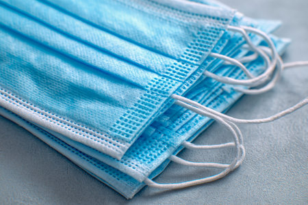 A neat pile of protective blue masks with elastic bands rests on a sleek surface, embodying...