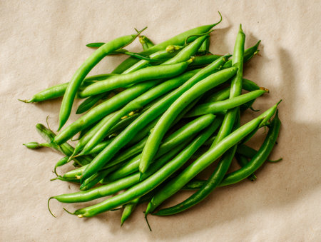 Vibrant green beans casually spread across a plain surface, exuding freshness and natural...