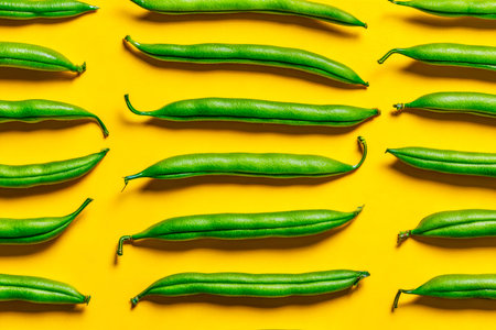 A crisp cluster of bright green beans lies neatly aligned against a lively yellow backdrop, creating...