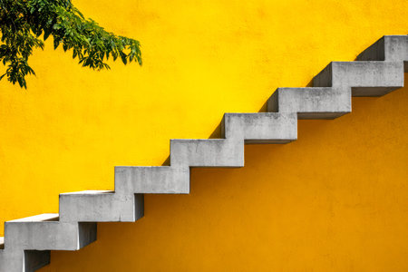 A sleek, minimalist staircase crafted from concrete rises alongside a bright yellow backdrop, adding...