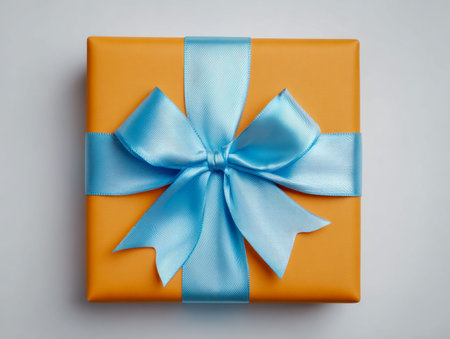 An exquisite orange parcel adorned with a flowing blue satin bow, set against a sleek gray backdrop...