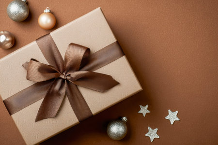 A sophisticated gift package wrapped with a velvety brown ribbon, nestled among shimmering metallic spheres, sparkling glittery adornments, and twinkling star accents onの写真素材