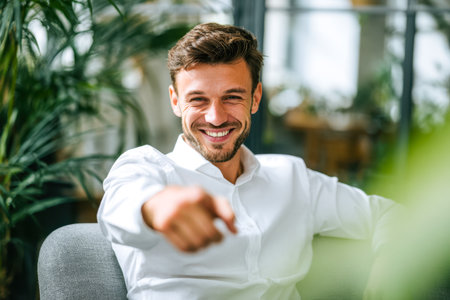 A self-assured young professional radiates enthusiasm while gesturing towards something inspiring in a sleek, contemporary workspace filled with natural light.のeditorial素材
