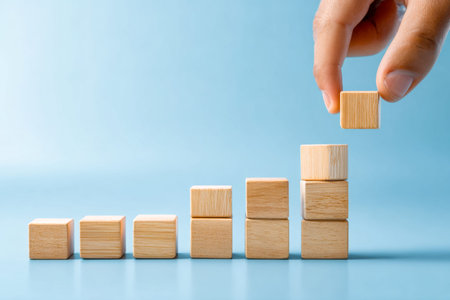 A person's hand carefully places wooden cubes in ascending order, representing development,...