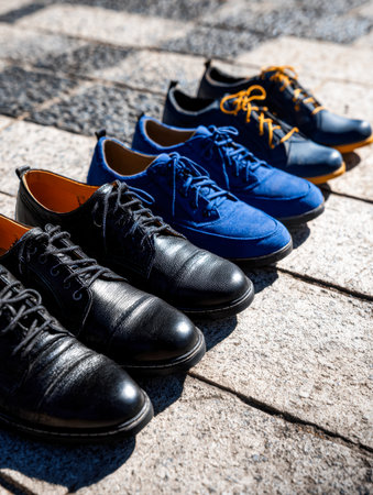 A trio of sleek black, blue, and navy shoes crafted from leather and canvas, artfully positioned on rustic stone paving, exuding casual elegance.の写真素材