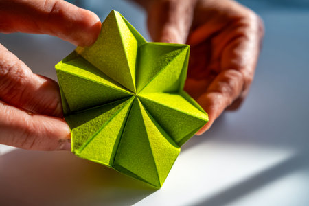 A vibrant green paper star with precise geometric folds is gently cradled in open hands, creating a...