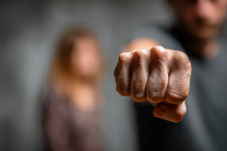 A sharply focused fist expresses raw intensity, while a softly blurred woman in the background hints at underlying turmoil and emotional strain.のeditorial素材