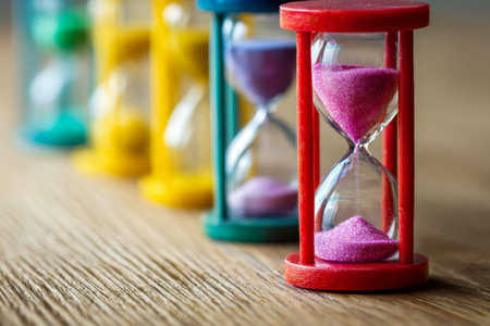 A row of old-fashioned hourglasses filled with vivid, differently shaded sands rests on a wooden...