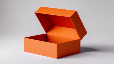 A vibrant orange cardboard box with a tactile surface, featuring a sturdy hinged lid flipped open, perfect for eye-catching gift wrapping or innovative displays.の写真素材