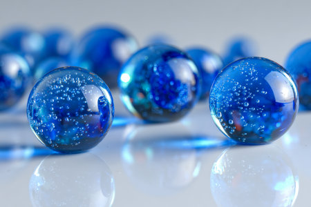 A collection of luminous blue glass spheres featuring a glossy finish, internal bubbles, and a mirrored sheen, artfully spread across a pristine white surface.の写真素材