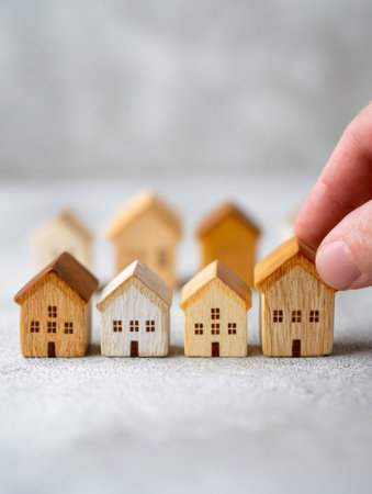 A hand carefully lines up tiny wooden dwellings on a rough surface, illustrating concepts of property choice, investment planning, and strategic development.の写真素材